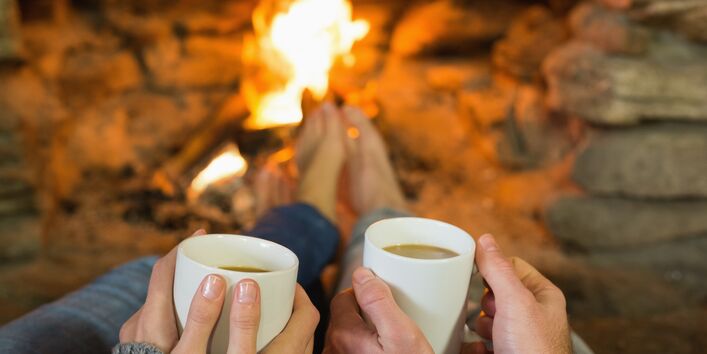 Zwei Menschen sitzen vor dem Kamin und halten Teetassen in der Hand.