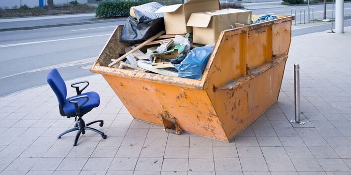 Ein Müllcontainer steht auf der Straße, daneben steht ein Bürostuhl