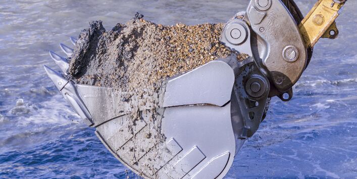 Excavator bucket with sediment in a river