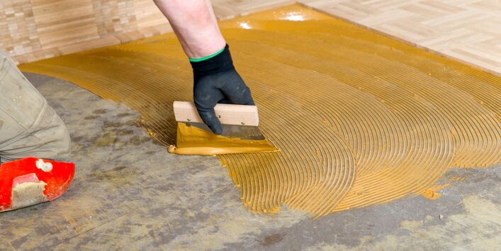 Ein Mann verarbeitet Bodenbelagsklebstoff.