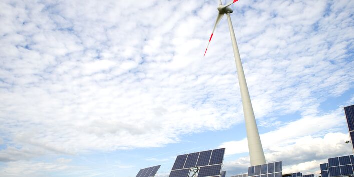 Photovoltaik- und Windenergieanlagen vor blauem Himmel mit Schäfchenwolken.