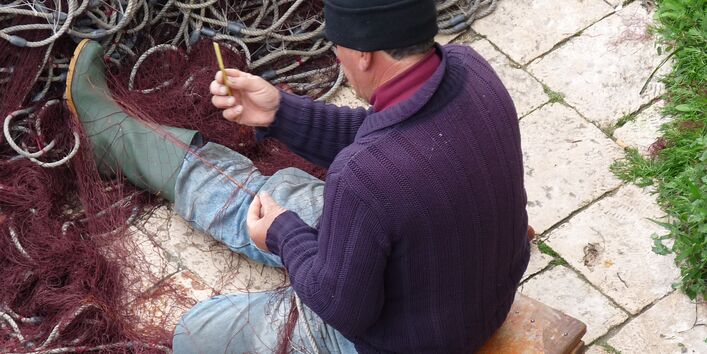 Rückenaufnahme eines Fischers, der Netze repariert.