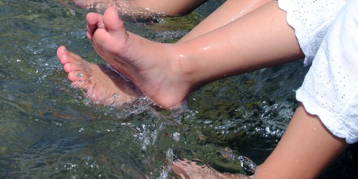 Füße von zwei Mädchen in weißen Kleidern in Wasserbecken.