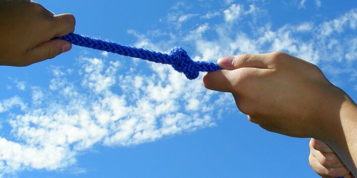 Blaues Seil mit Knoten an dem von Händen in verschiedene Richtungen gezogen wird.