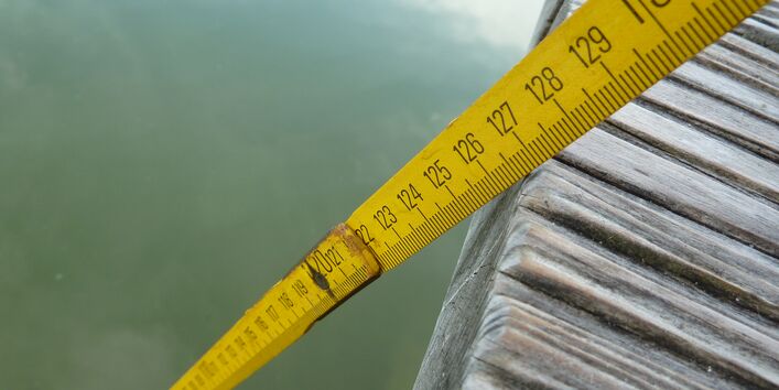 Nahaufnahme gelber Zollstock, der von einem Bootssteg ins Wasser reicht.