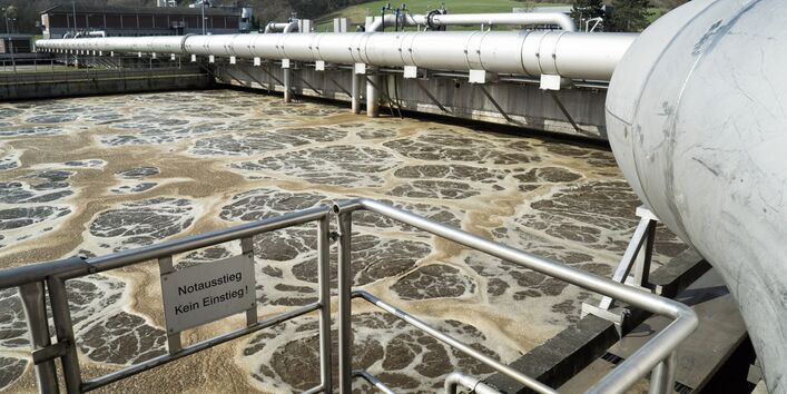 Ein Rohr mit einem Warnschild "Notausstieg - Kein Einstieg" an einem Klärbecken einer Kläranlage.