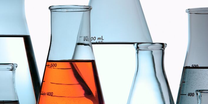 Verschiedene Erlenmeyerkolben, die mit farbloser und roter Flüssigkeit gefüllt sind, spiegeln sich im glatten Boden