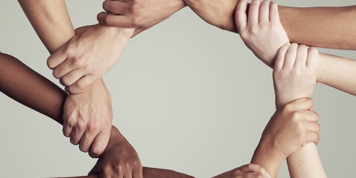 Hände verschiedener Hautfarbe halten sich fest und bilden einen Kreis.