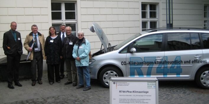 A group of persons standing beside a silver VW Touran with the inscription "R744"