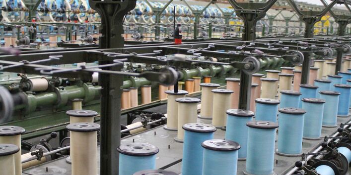 Die Mechanik einer Spinnerei mit vielen hintereinander aufgereihten Garnrollen in blau und beige