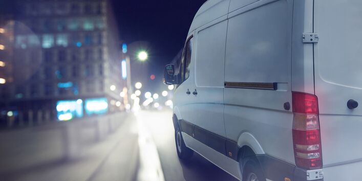 Ein Lieferwagen fährt bei Dunkelheit durch eine Stadt.