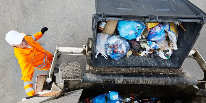 Ein Müllcontainer wird in einen Müllwagen gekippt.