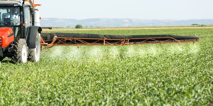Ein Traktor sprüht Pflanzenschutzmittel auf ein Feld.