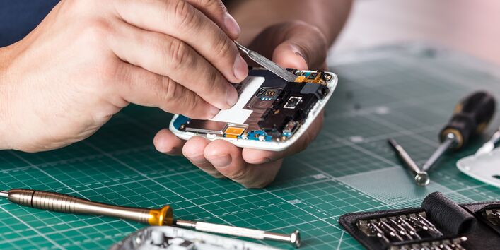 Eine Hand hält ein Smartphone, welches repariert wird.