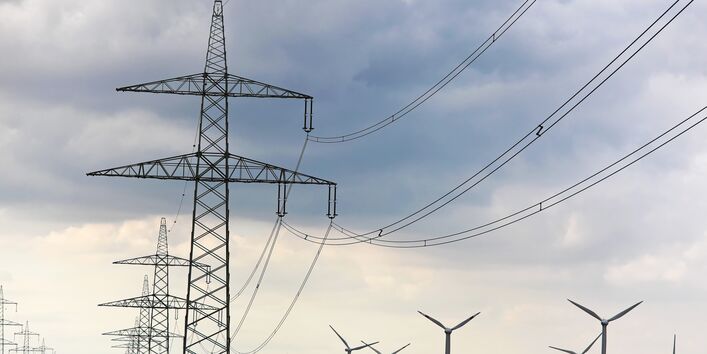 Ein Strommast mit Leitungen vor blauem Himmel.