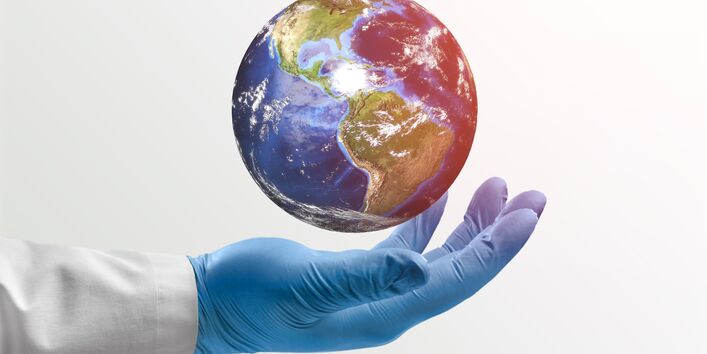 Foto eines Arms mit Arztkittel und Handschuhen, der einen Erdball hält.