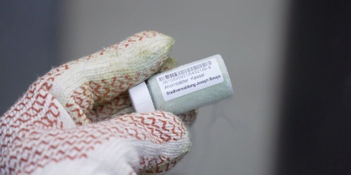 Hand mit Handschuh hält eine Probe in einem kleinen Fläschchen.