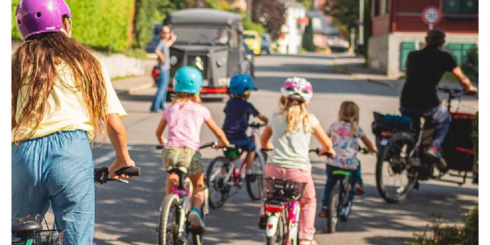 Zwei Erwachsene sowie vier Kinder fahren mit Fahrrädern auf der Straße