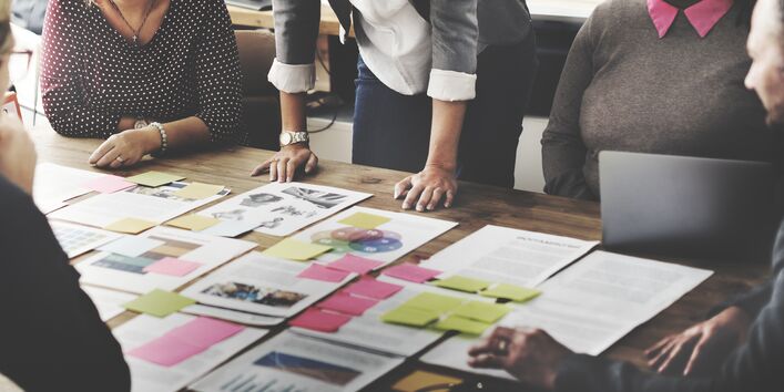 Teamsitzung, auf dem Tisch sind viele Unterlagen und bunte Klebezettel verteilt