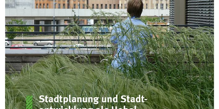 Mensch sitzt in hohem Gras und schaut auf eine Baustelle in der Stadt