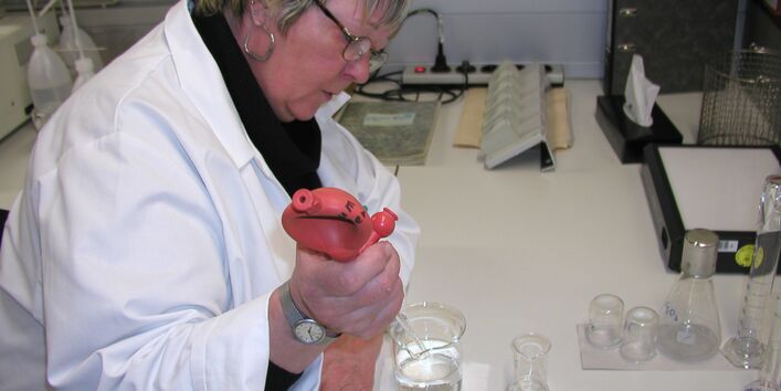 Eine Mitarbeiterin des Umweltbundesamtest sitzt an einem Labortisch. Sie setzt mit einer großen Pipette Wasserflöhe in Testgefäße ein. 