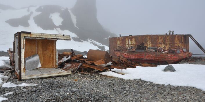 Auf einem Strandabschnitt liegt rostiger Schrott. Im Hintergrund erhebt sich ein Berg, der von Nebel verhüllt wird.