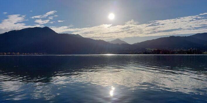 The picture shows a mountain lake in glaring sunlight. A mountain chain is visible in the background.