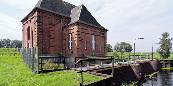 The picture shows the pumping station Steinschleuse on the Eider river. A retaining wall with a bridge and a brick-built house are visible.