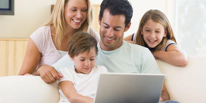 Familie sitzt auf dem Sofa und schaut zusammen auf den geöffneten Laptop