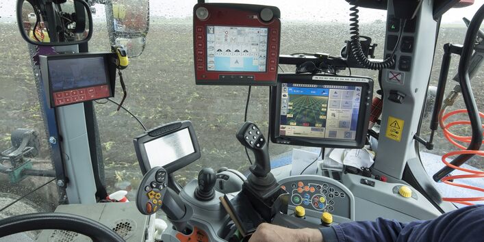 Blick durch die verregnete Windschutzscheibe eines Traktors mit GPS und Computermonitor auf ein Kartoffelfeld.
