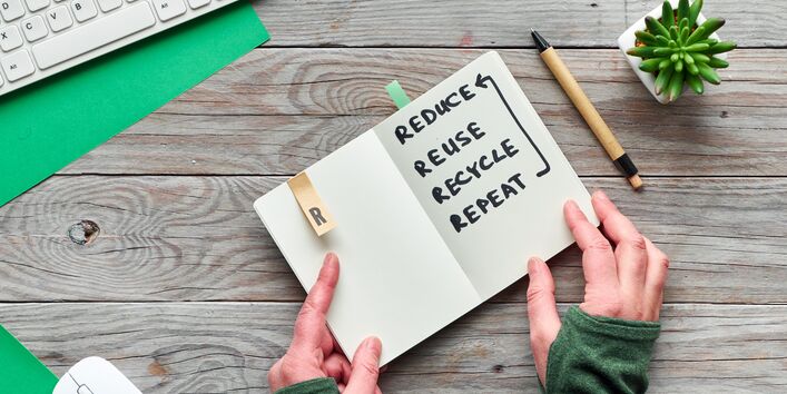 Ein Bild mit einem Notizbuch auf dem Wörter geschrieben sind. Diese lauten reduce, reuse, recycle, repeat. Auf deutsch: reduzieren, wiederverwenden, recyceln, wiederholen. 