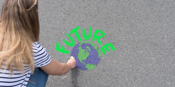 Symbolbild für den Klimaschutz. Weibliche Person malt mit Kreide die Erde und das Wort Future auf den Boden. 