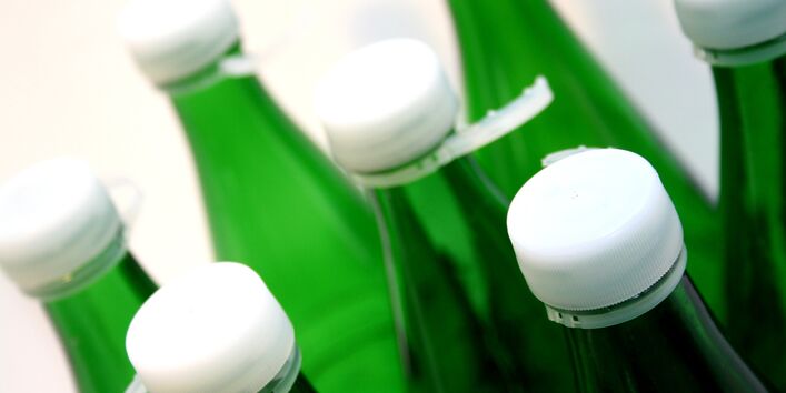 Zu sehen sind mehrere grüne Mehrwegflaschen, vermutlich Wasserfalschen. Die Flaschen haben alle einen Deckel und waren bereits geöffnet. 