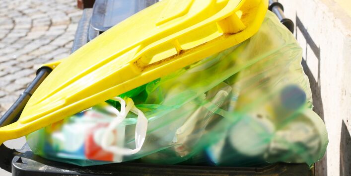 Eine überfüllte Mülltonne für Plastikabfälle, die leicht geöffnet ist, weil diese mit gefüllten Müllbeuteln voll ist. 