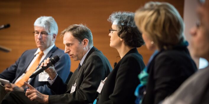 Personen sitzen zur Interviewrunde. Ein Teilnehmer hält das Mikrofon in der Hand und spricht hinein.