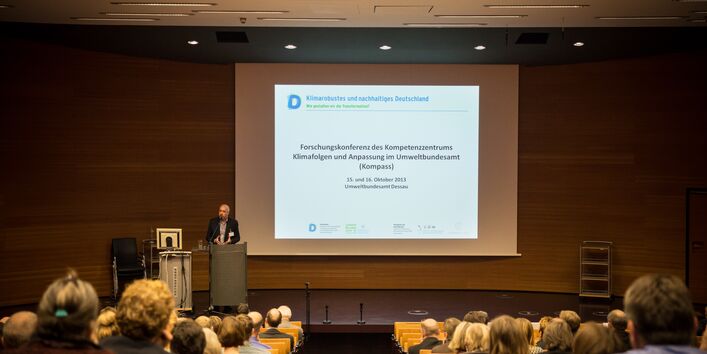 Ein Vortragender steht vor dem Hintergrund der Präsentation am Rednerpult