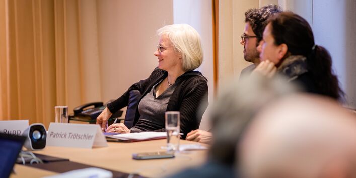 Teilnehmende sitzen im Workshopraum zusammen und schauen zuhörend in eine Richtung in einem hellen Raum.