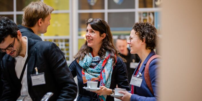 Teilnehmende stehen in der Pause mit Kaffetassen in den Händen beisammen und sprechen lachend miteinander.