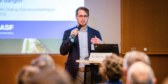 Vortragender steht mit Mikrofon in der Hand am Stehpult. Im Hintergrund ist seine Präsentation abgebildet.