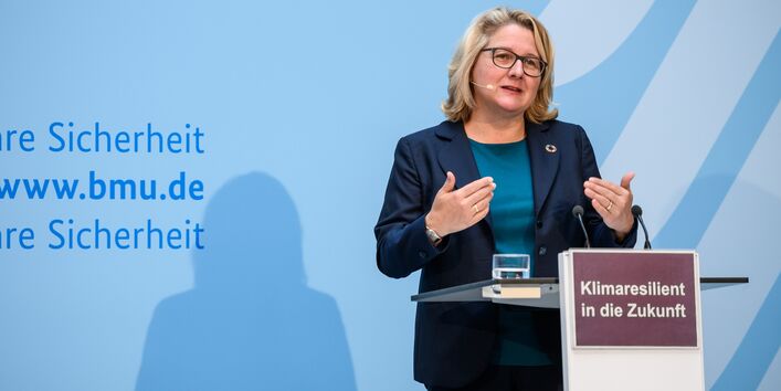 Die Umweltministerin steht am Rednerpult vor blauem Hintergrund und trägt gestikulierend vor.
