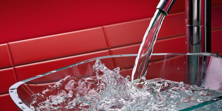Laufender Küchenwasserhahn mit Glasschale, roter Hintergrund