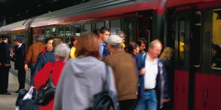 Zug im Bahnhof mit Menschengruppen am Gleis