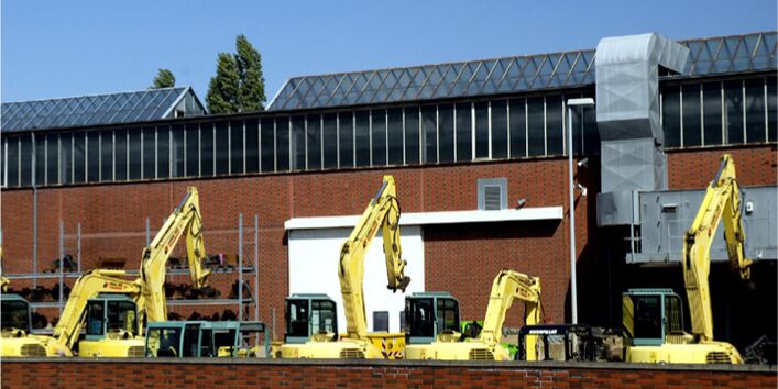 Fünf Bagger stehen auf einer Gewerbefläche vor einer Industriehalle