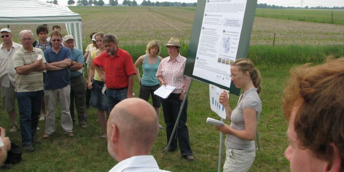 Menschen stehen auf Rasen um eine Präsentationstafel herum