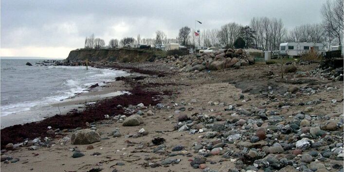 Seewasser spült an den Strand, im Hintergrund befinden sich Bäume und ein Campingplatz