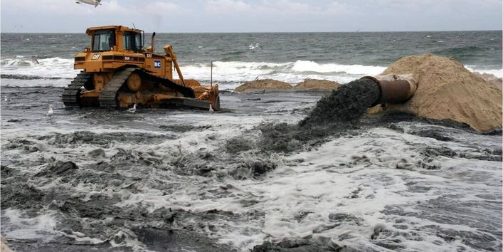 Ein Bagger verteilt Sand am Spülsaum, im Vordergrund entweicht Sand aus einem Rohr