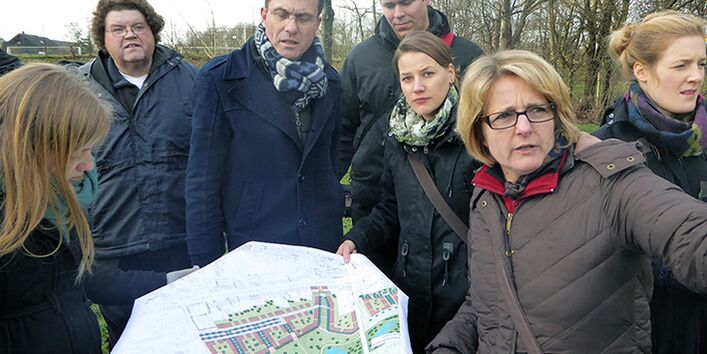 Das Projektteam hält gemeinschaftliche eine Karte des zukünftigenOstparks in den Händen und schauen abwechseln auf die Karte und in die Richtung, wo sich das Ziel befindet. Im Hintergrund befinden sich unbelaubte Bäume. Die Personen sind warm angezogen.