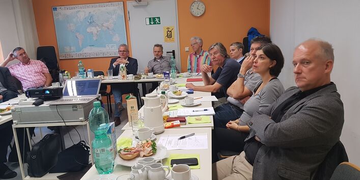 Mehrere Personen sitzen gemeinsam an einem Tisch und folgen einer Präsentation.