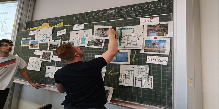 Praktische Erprobung in einer Berufsschule. Zwei Menschen stehen an einer Magnet Schultafel und sortieren Projektbilder.