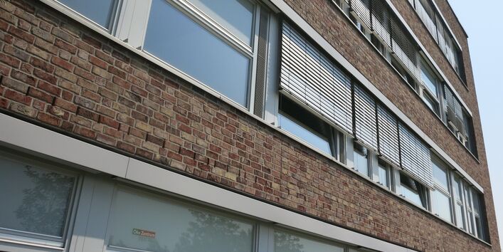 Ein vierstöckiges Haus mit großen Fenstern und Sonnenrollos